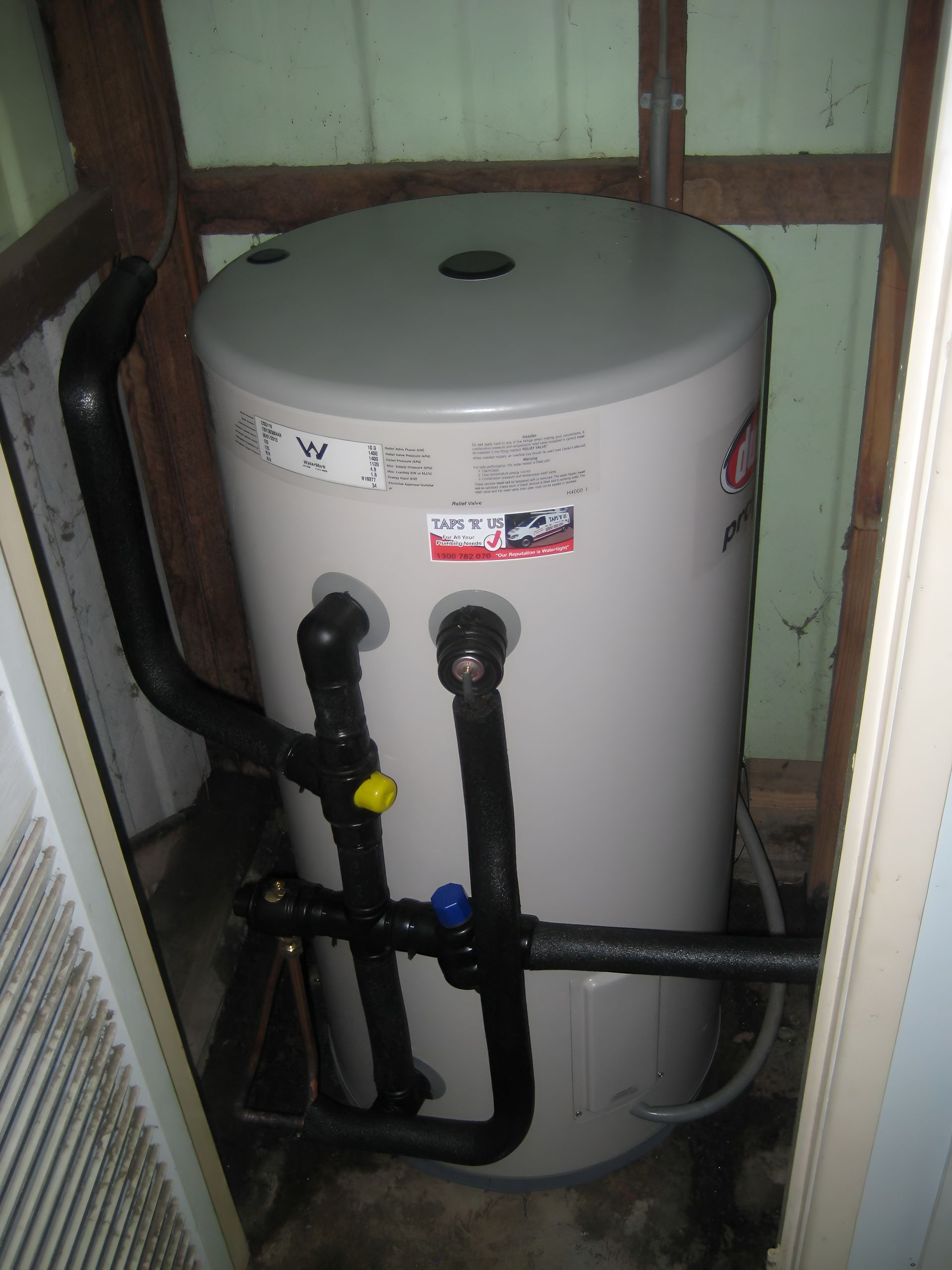 A Cylindrical, Beige Water Heater With Black Pipes in a Small Enclosure — Taps 'R' Us in Sippy Downs, QLD