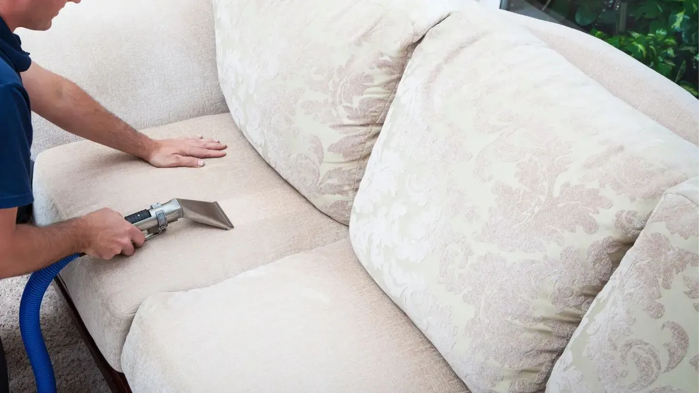 Person cleaning beige sofa with a steam cleaner.