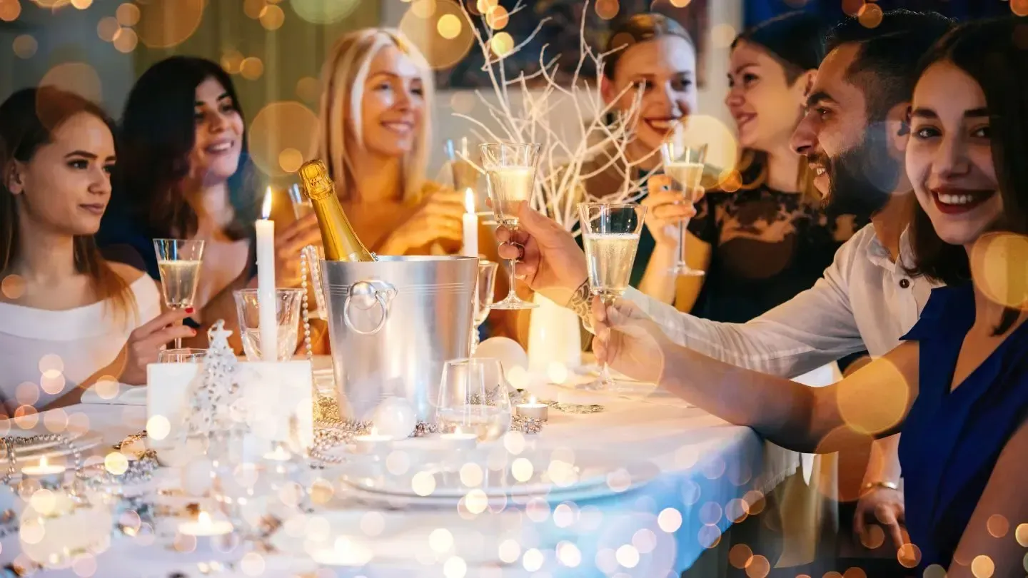 People toasting with champagne around a festive table with candles and lights.