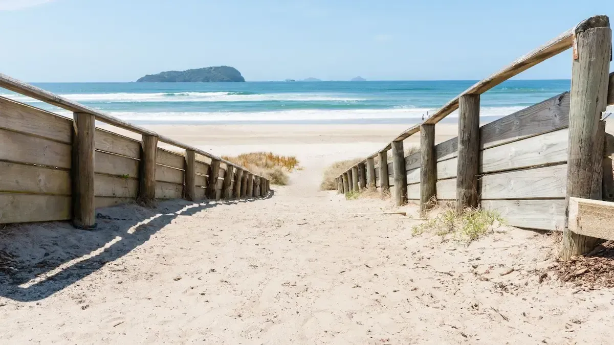 Wooden boardwalk leading to a sandy beach and ocean, with a small island visible in the distance.