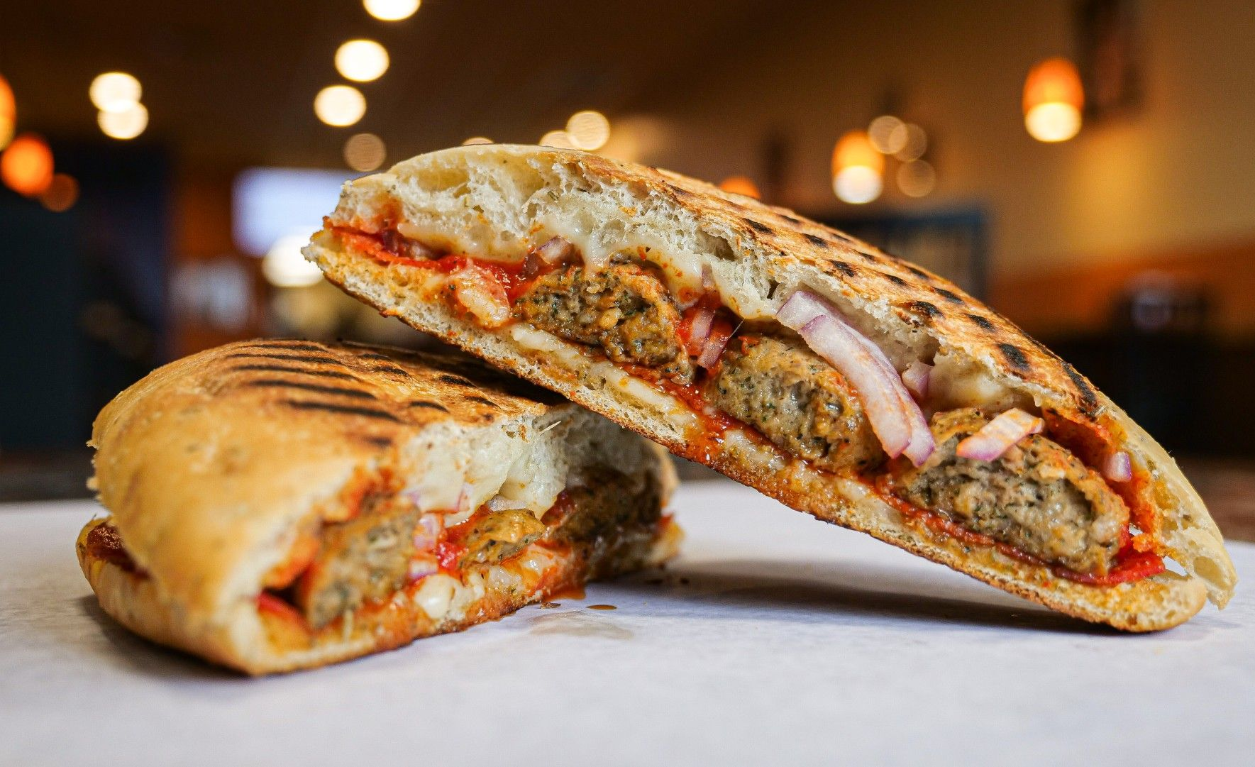 A grilled sandwich is cut in half on a piece of wax paper