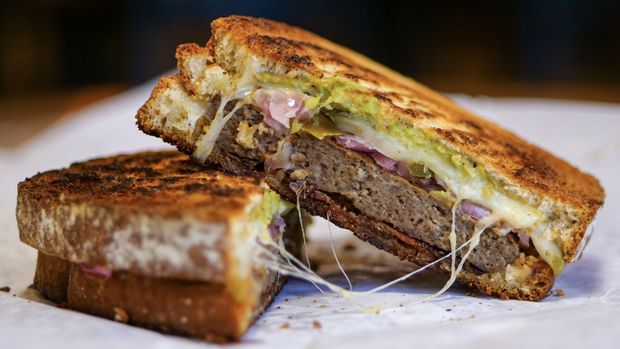 A grilled sandwich is cut in half on a piece of wax paper