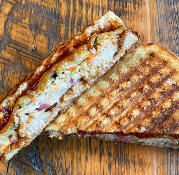 A grilled sandwich is cut in half on a piece of wax paper