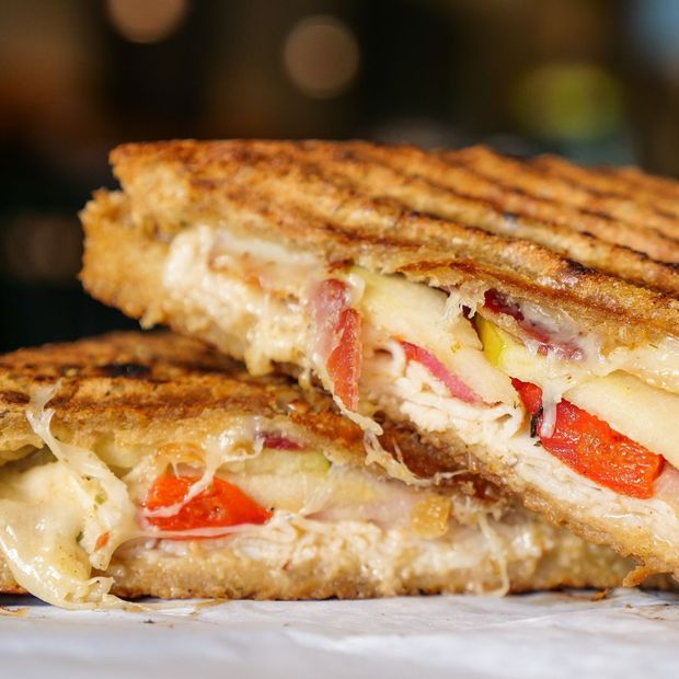 A grilled sandwich is cut in half on a piece of wax paper