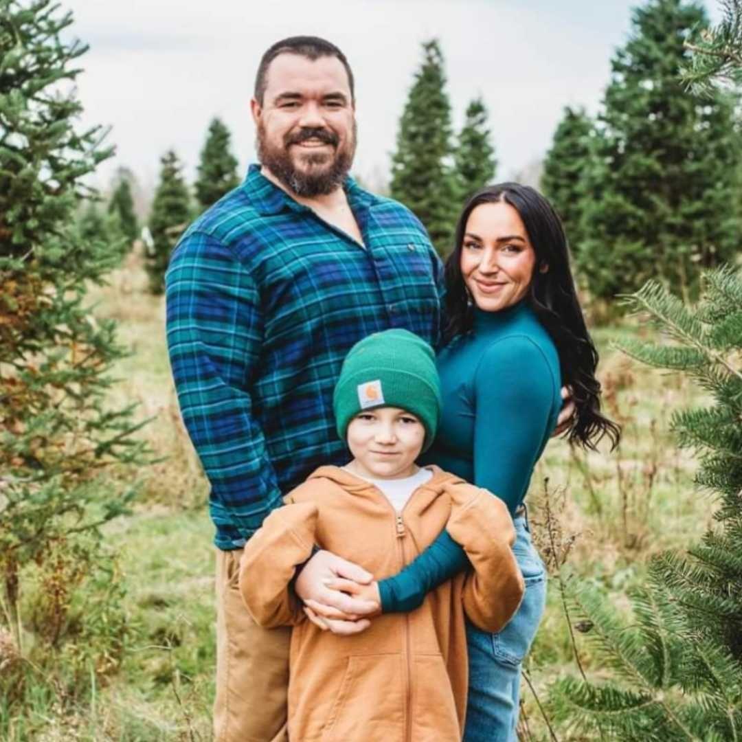 A man , woman and child are posing for a picture in a field of christmas trees.