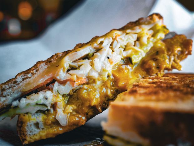 A grilled sandwich is cut in half on a piece of wax paper