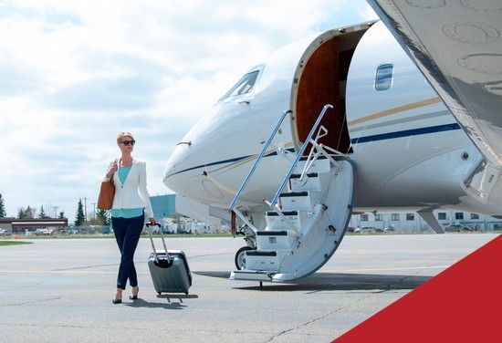 Woman stands beside a private jet on a tarmac with rolling luggage.
