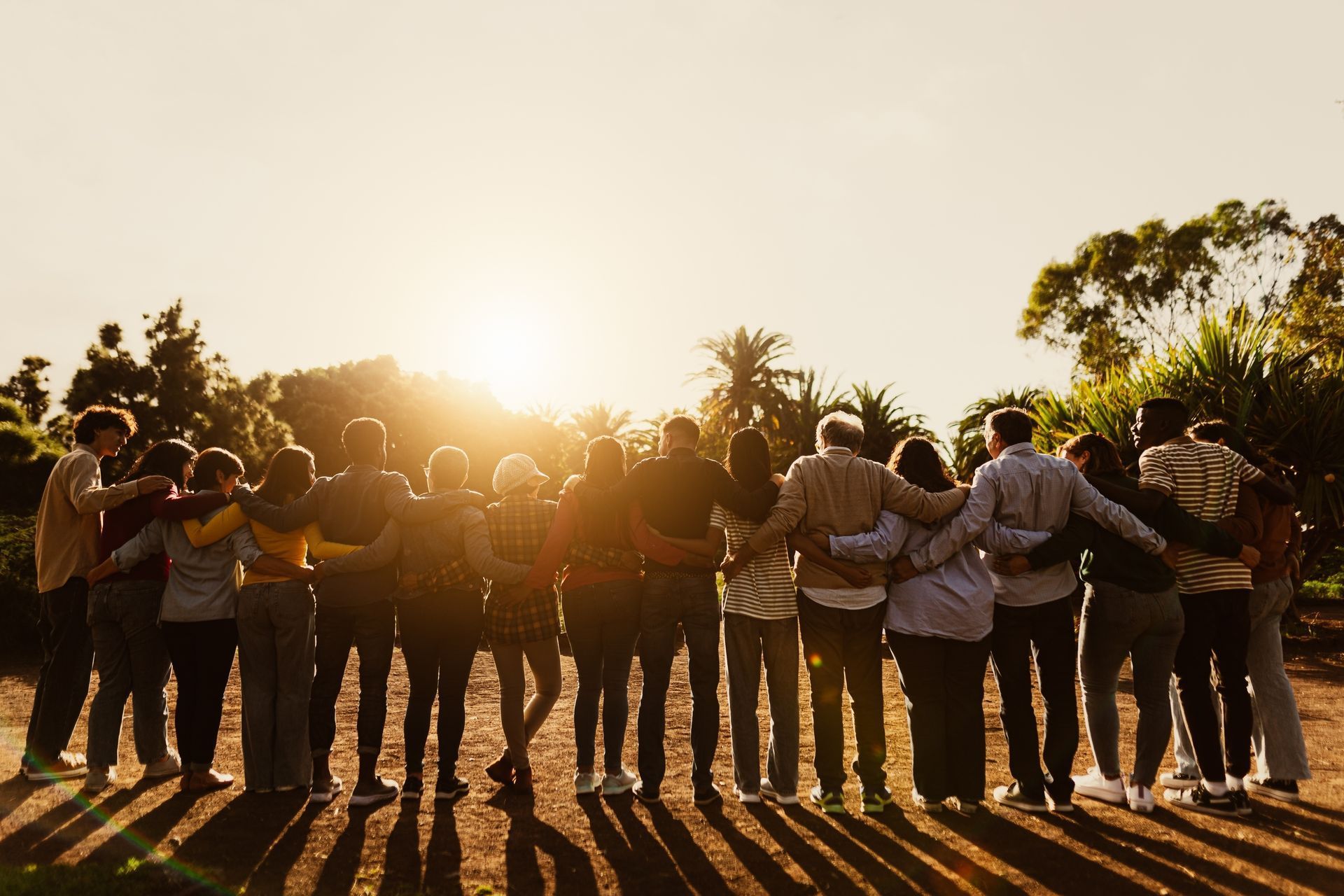 People with arms around each other, silhouetted against a bright sunset.
