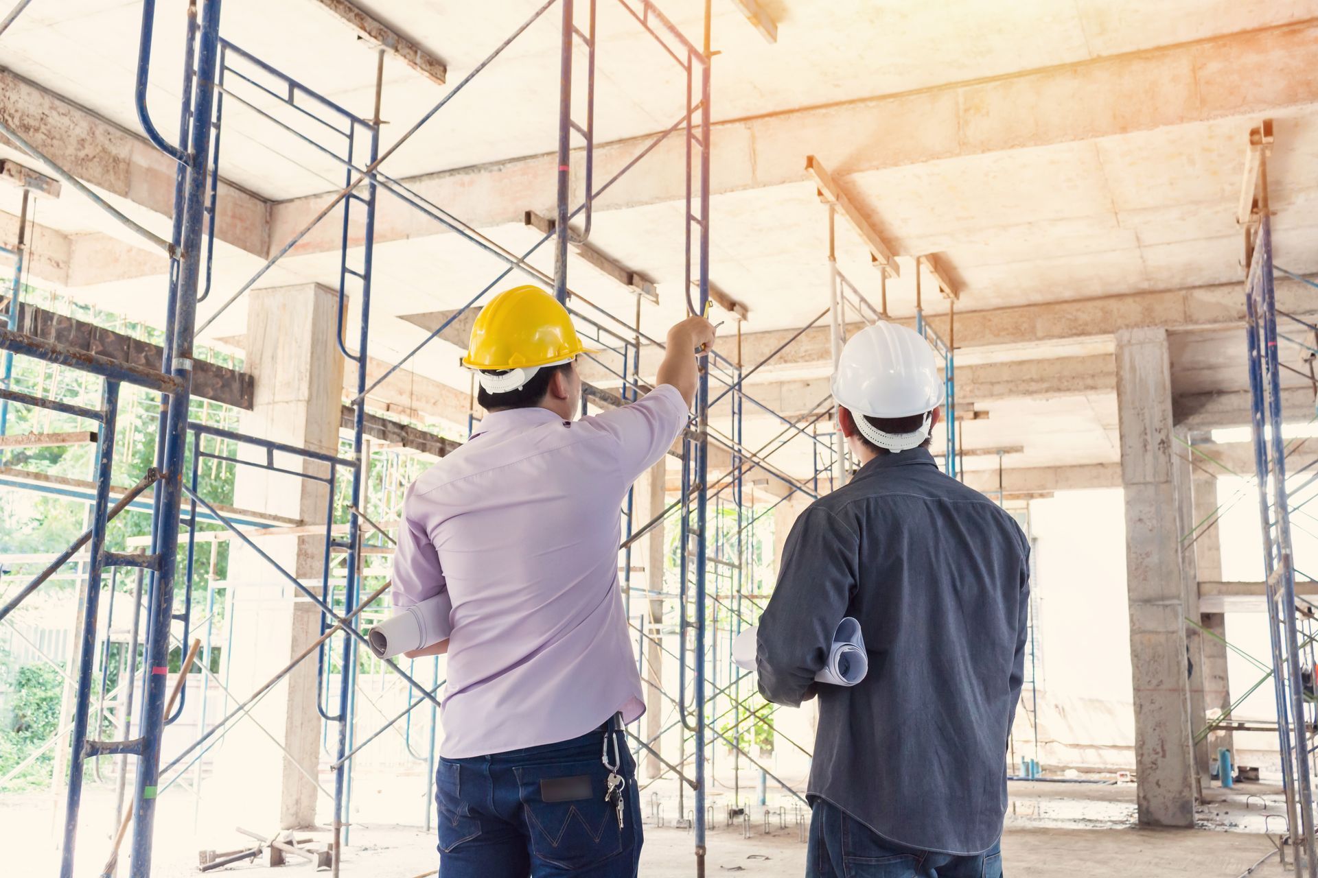 Two construction workers are standing in a building under construction.