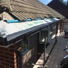 Roof repair on a house with white weatherproof membrane and blue tape along the eaves