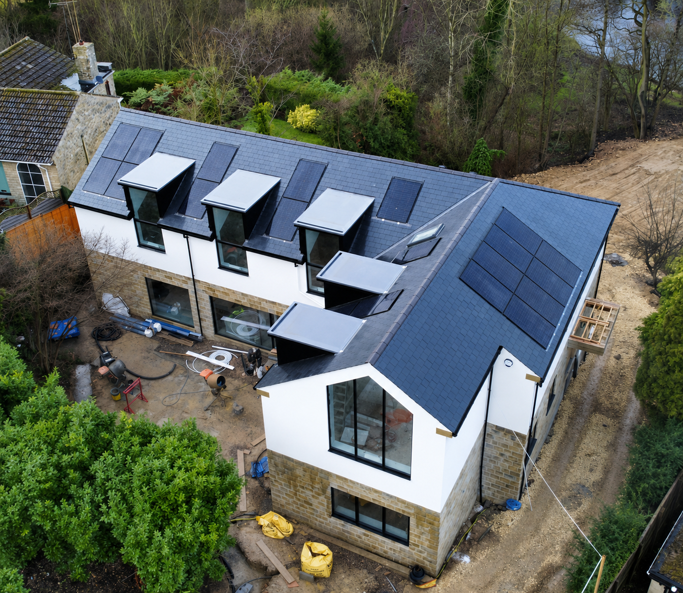 Aerial view of a modern house with blue solar-panel roof, dormer windows, and a backyard garden.