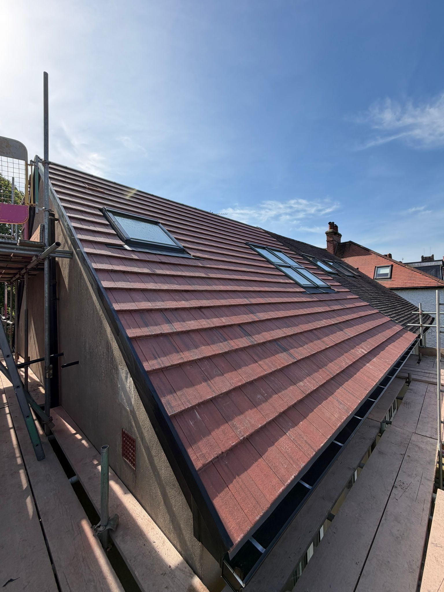 Rooftop with red tiles and a skylight under a blue sky, viewed from a narrow alley