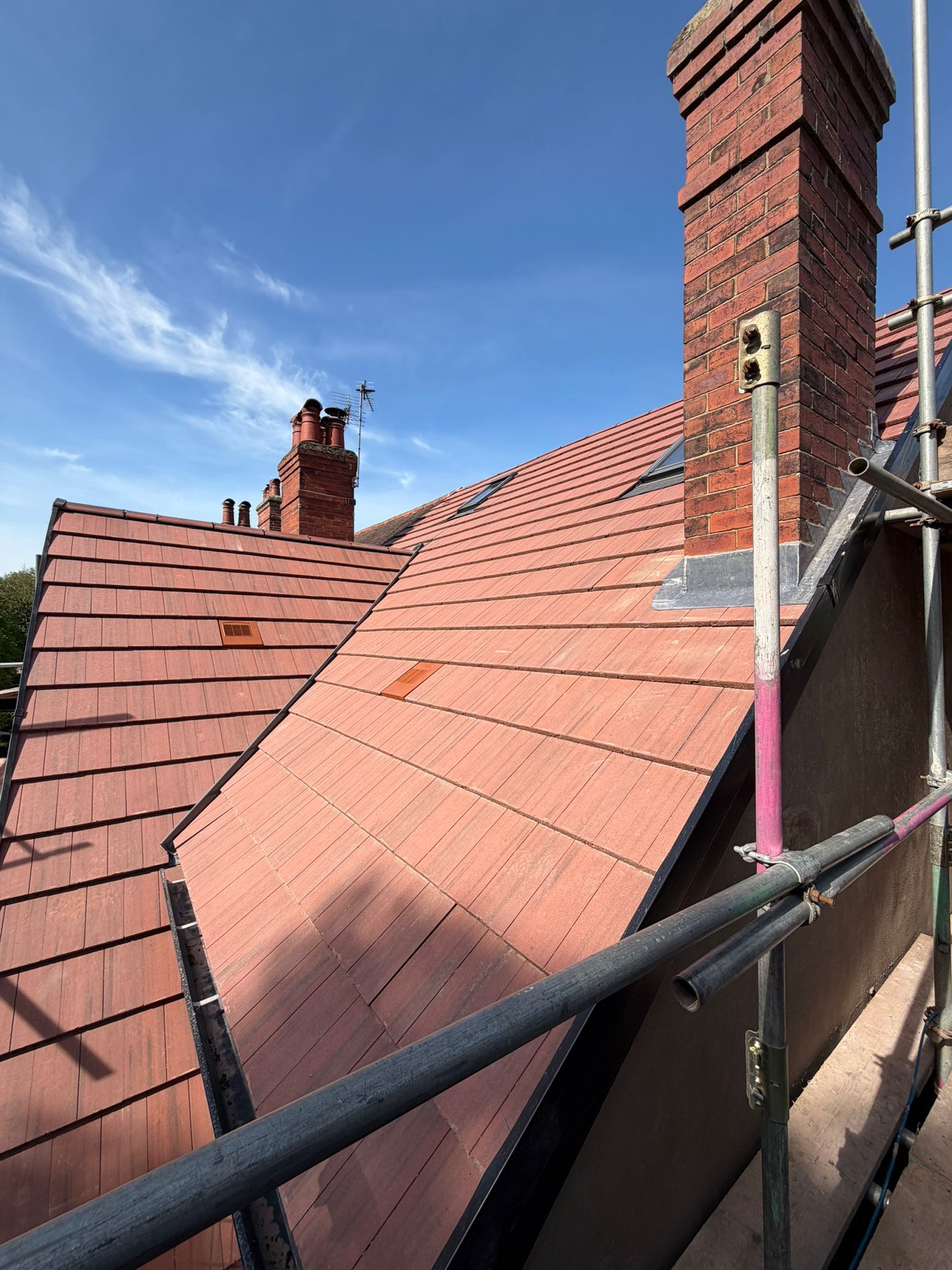 Rooftop with red tile shingles, brick chimney, and scaffolding under a blue sky