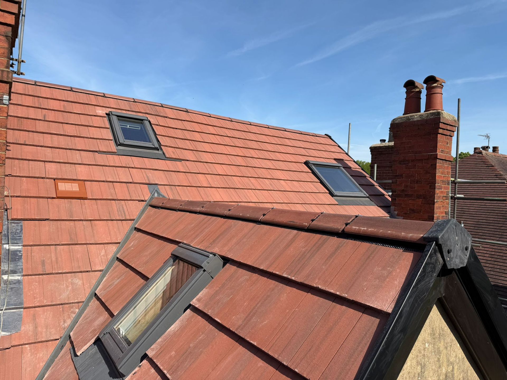 Red tiled rooftops with skylights and brick chimneys under a blue sky