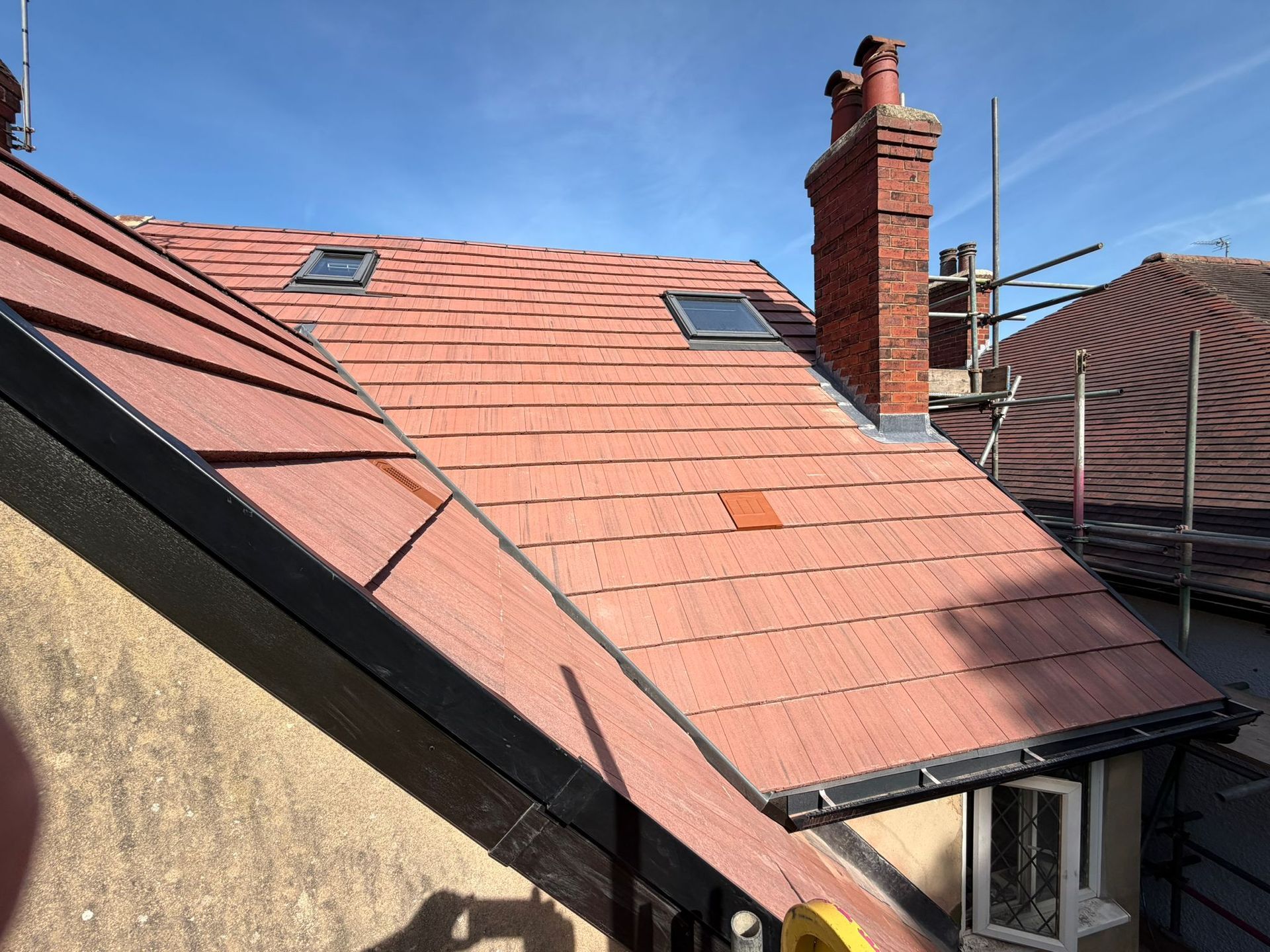 Red-tiled house roof with two skylights, a chimney, and blue sky above.