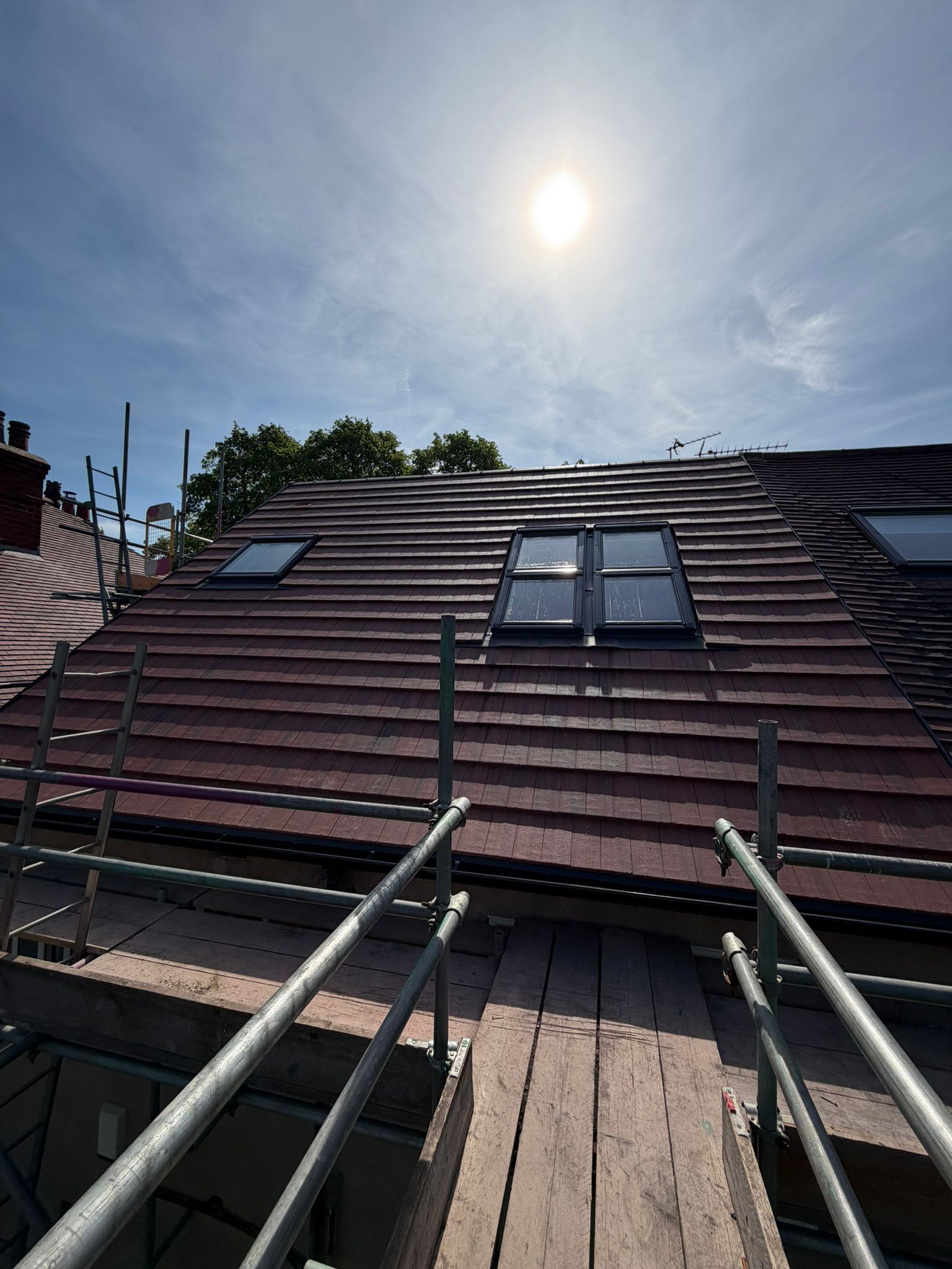 Red tiled roof with skylights and railings under a bright sun and blue sky