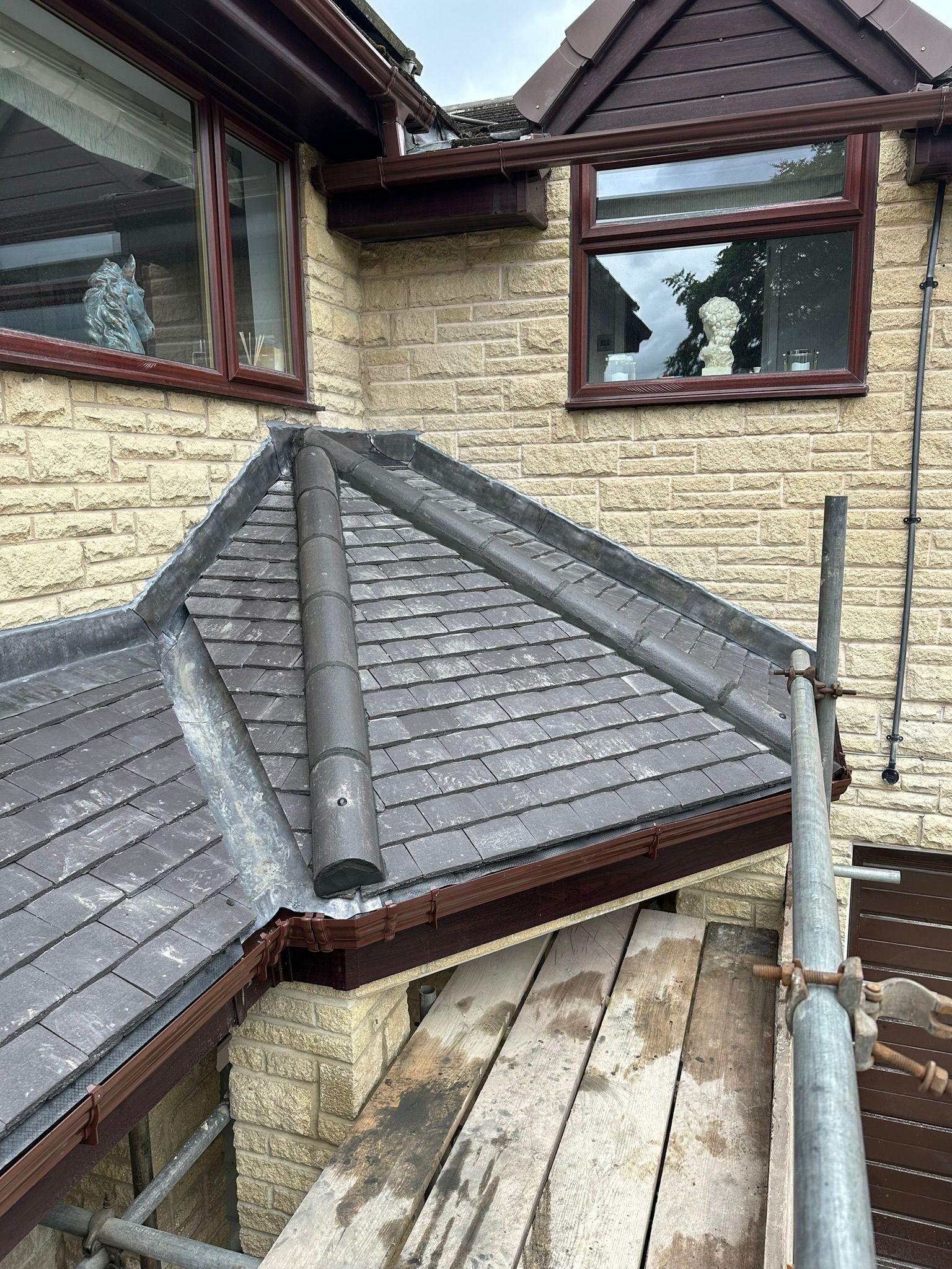 Rooftop with gray slate tiles, a metal vent pipe, and brick walls beneath dormer windows