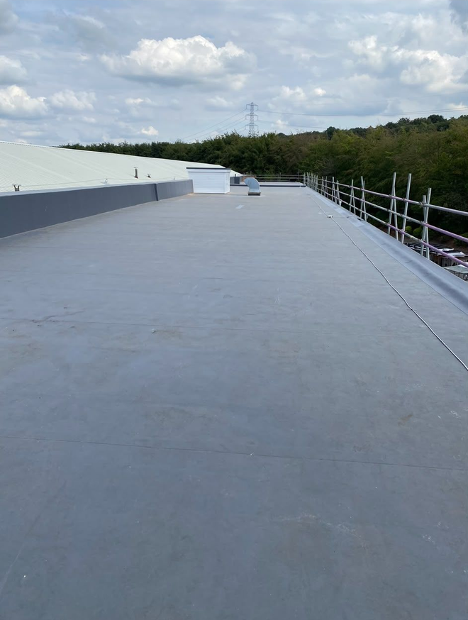 Wide rooftop walkway with gray surface, white structures, and railings beside trees under a cloudy sky