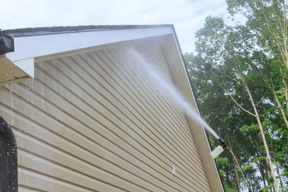 A person is using a high pressure washer to clean the side of a house.