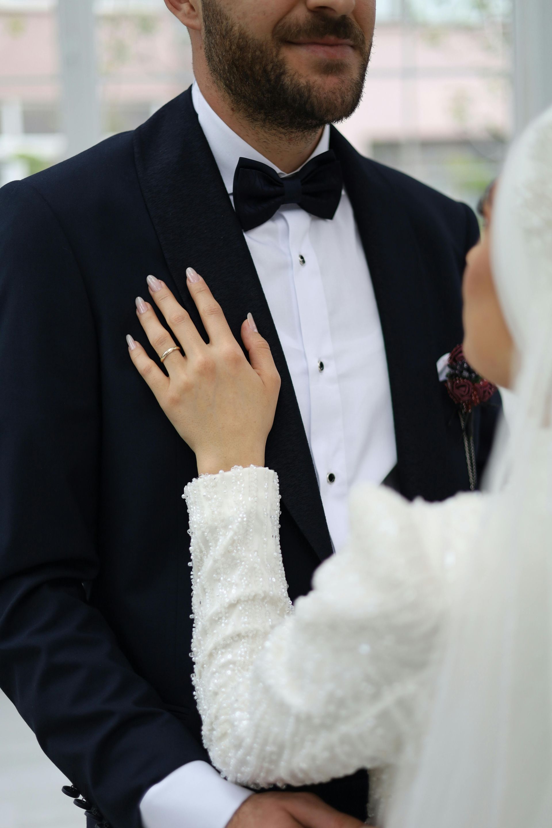 A bride and groom are standing next to each other and the bride is touching the groom 's jacket.