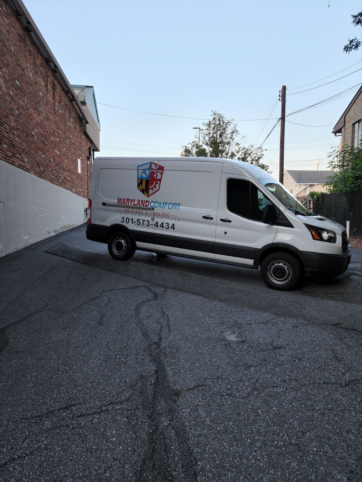 A white van is parked in a parking lot next to a brick building.