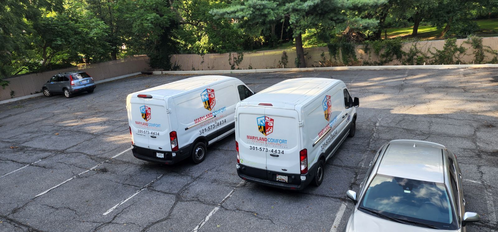 Three white vans are parked in a parking lot.