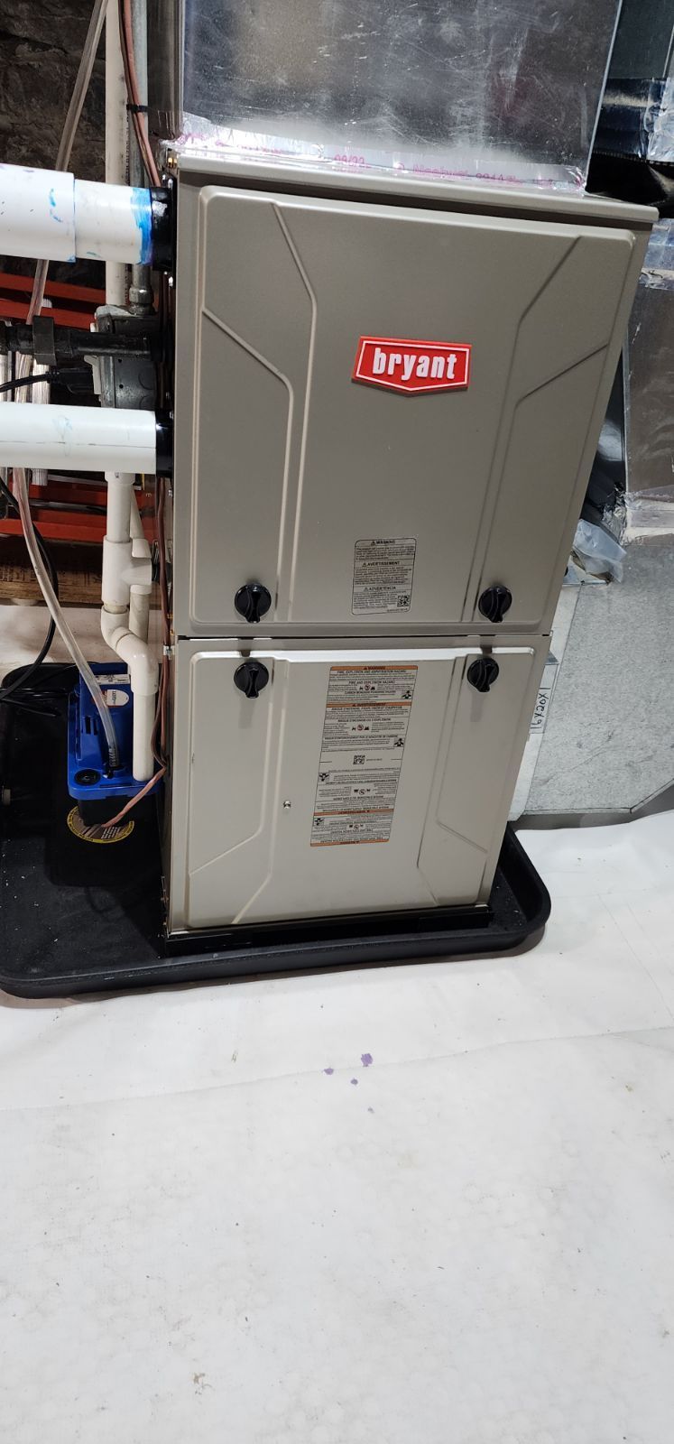 A lynx furnace is sitting on a tray on the floor in a basement.