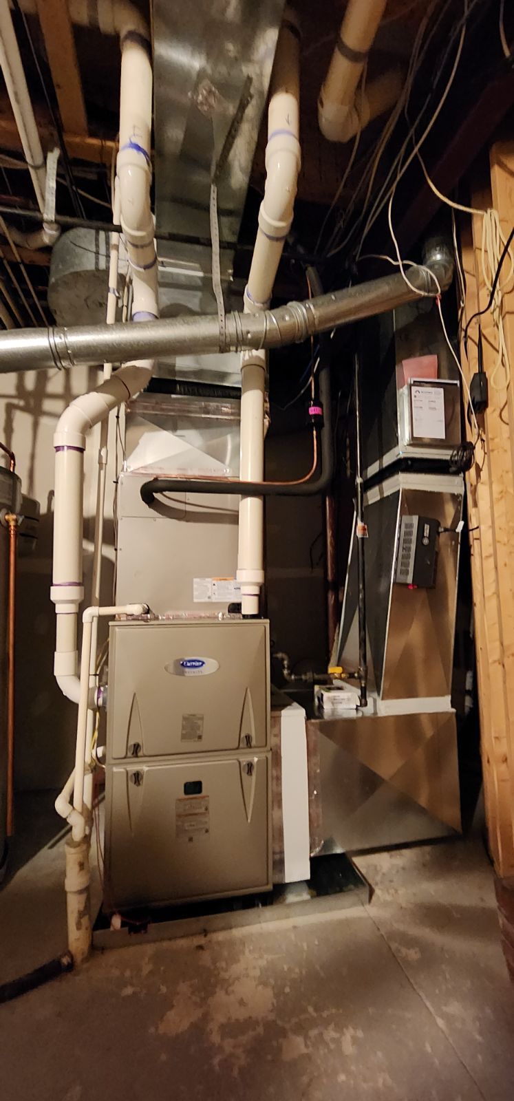A basement with a furnace , air conditioner , and pipes.