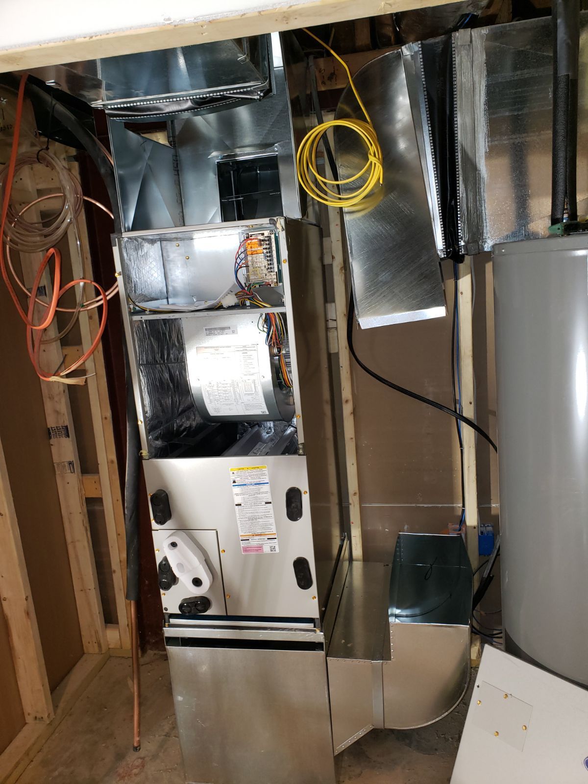 A stainless steel air conditioner is sitting in a room next to a water heater.