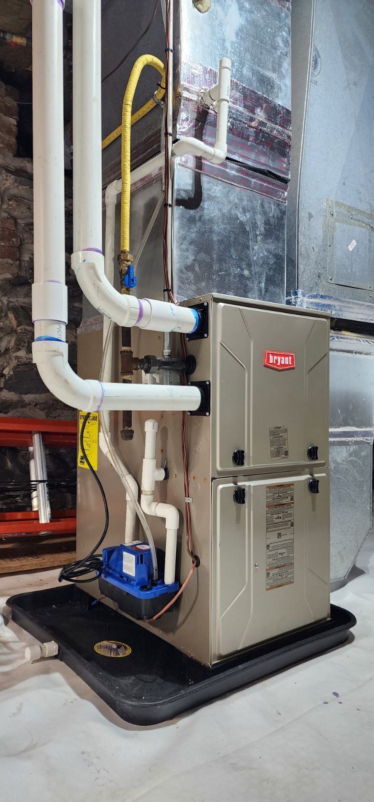 A furnace is sitting on top of a black mat in a basement.
