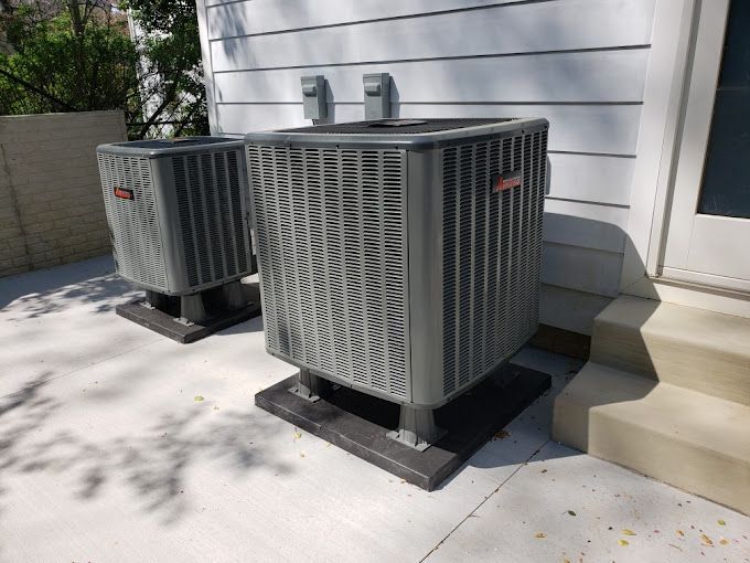 Two air conditioners are sitting on the side of a house.