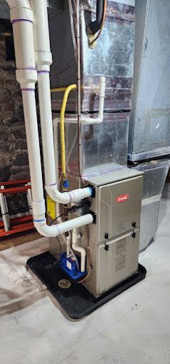 A furnace is sitting in a basement next to a ladder.