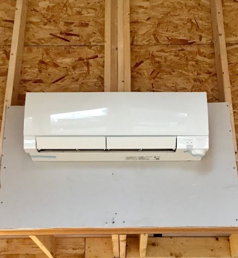 A white air conditioner is hanging from the ceiling of a wooden structure.