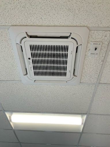 A white air conditioner is mounted to the ceiling of a room.