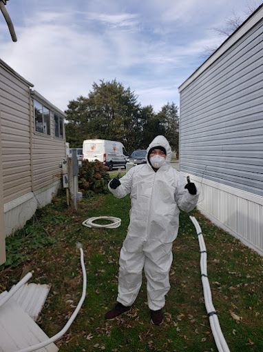 A man in a protective suit is standing in front of a mobile home.