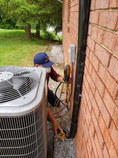 A man is working on an air conditioner on the side of a brick building.