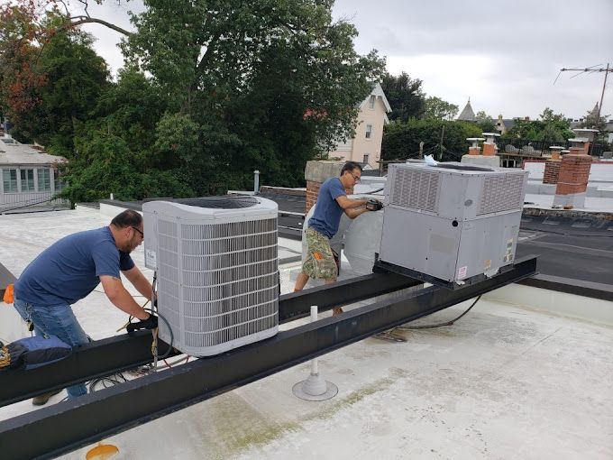 Two men are working on a rooftop air conditioner.