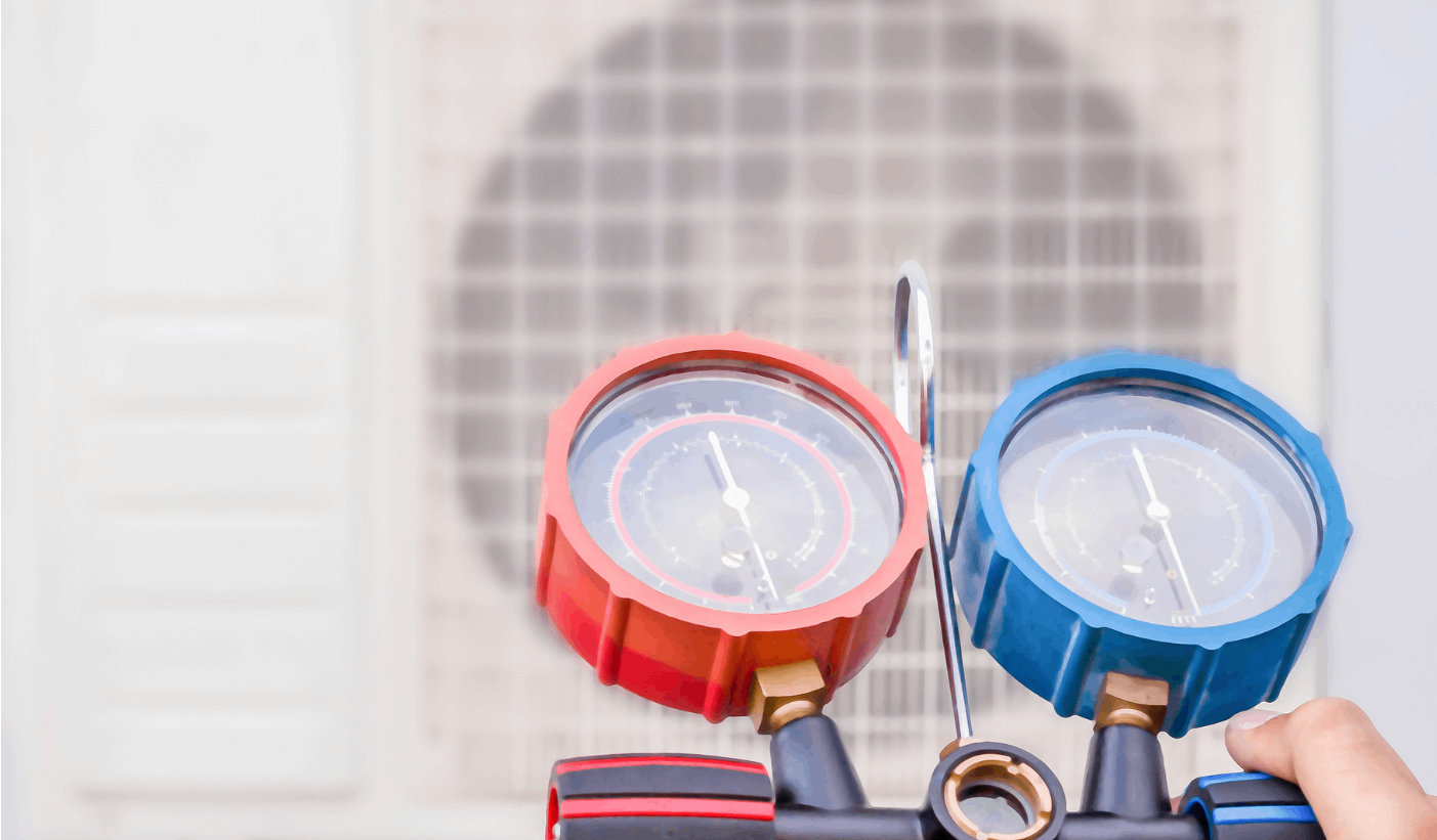 A person is holding a pressure gauge in front of an air conditioner.