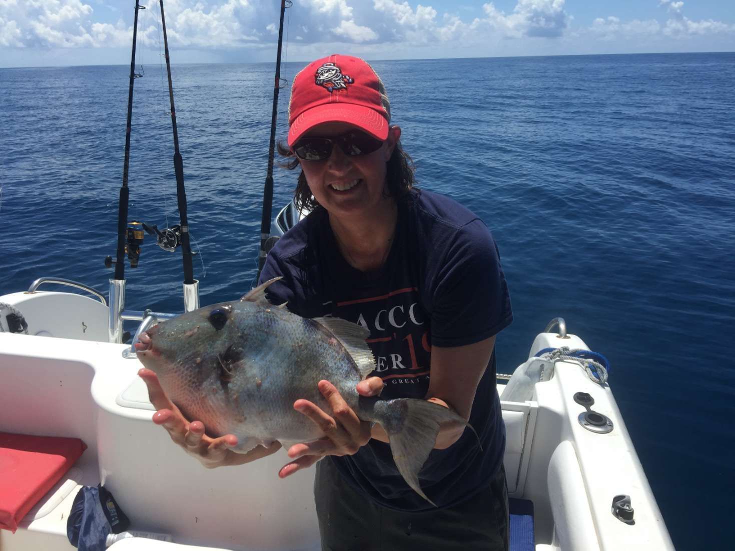 A woman is holding a large fish on a boat in the ocean.