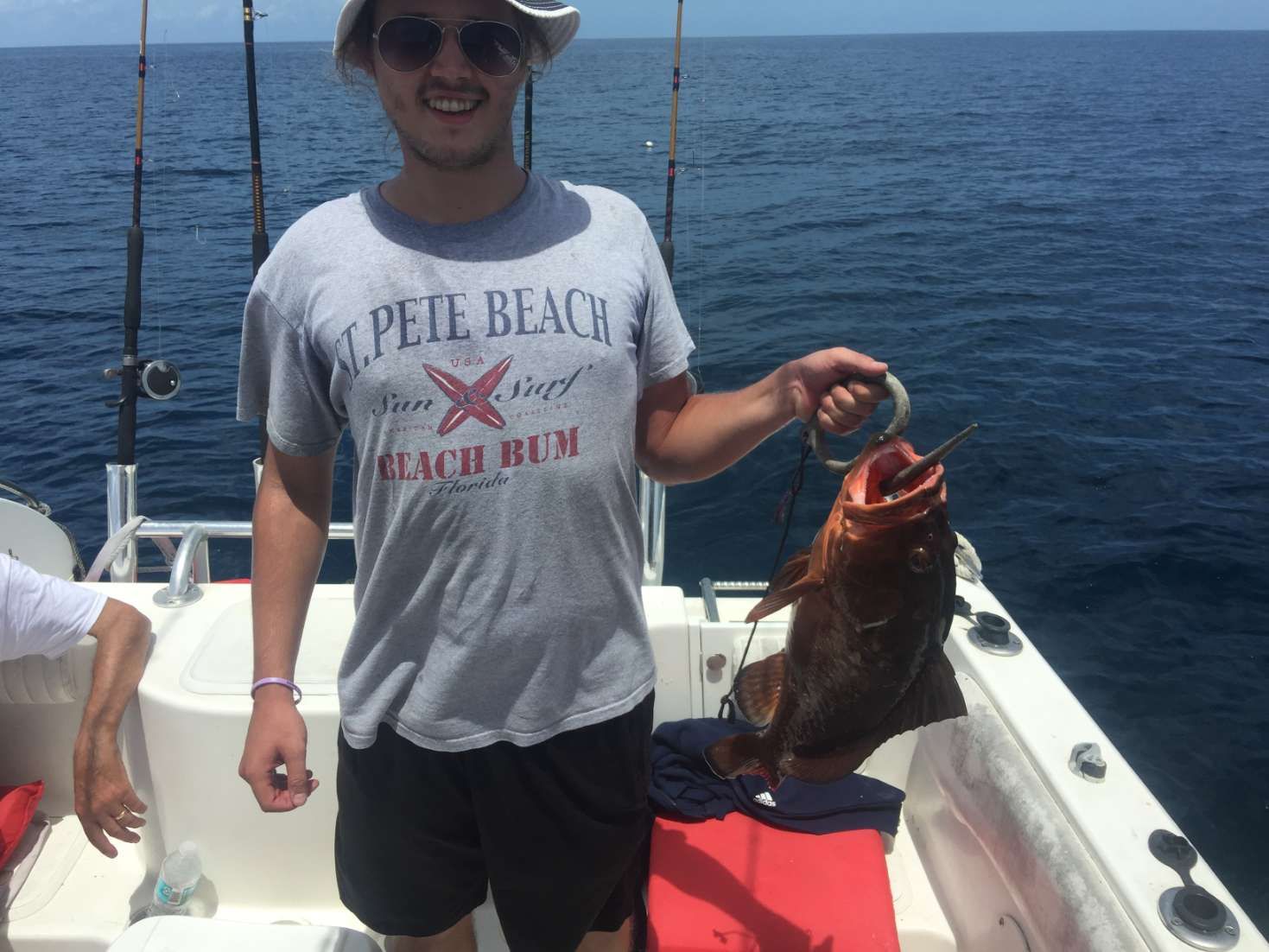 A man in a pele beach shirt is holding a fish on a boat