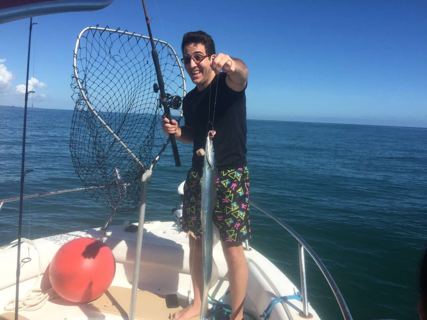A man is standing on a boat holding a fishing rod and a fish.