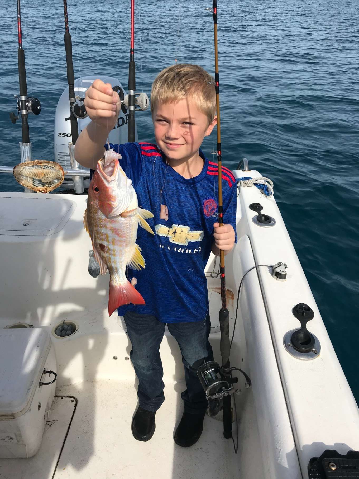 A young boy is holding a fish on a boat.