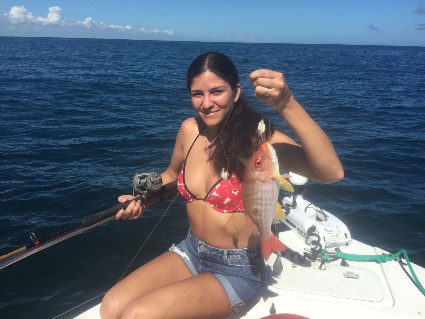 A woman in a bikini is sitting on a boat holding a fish.