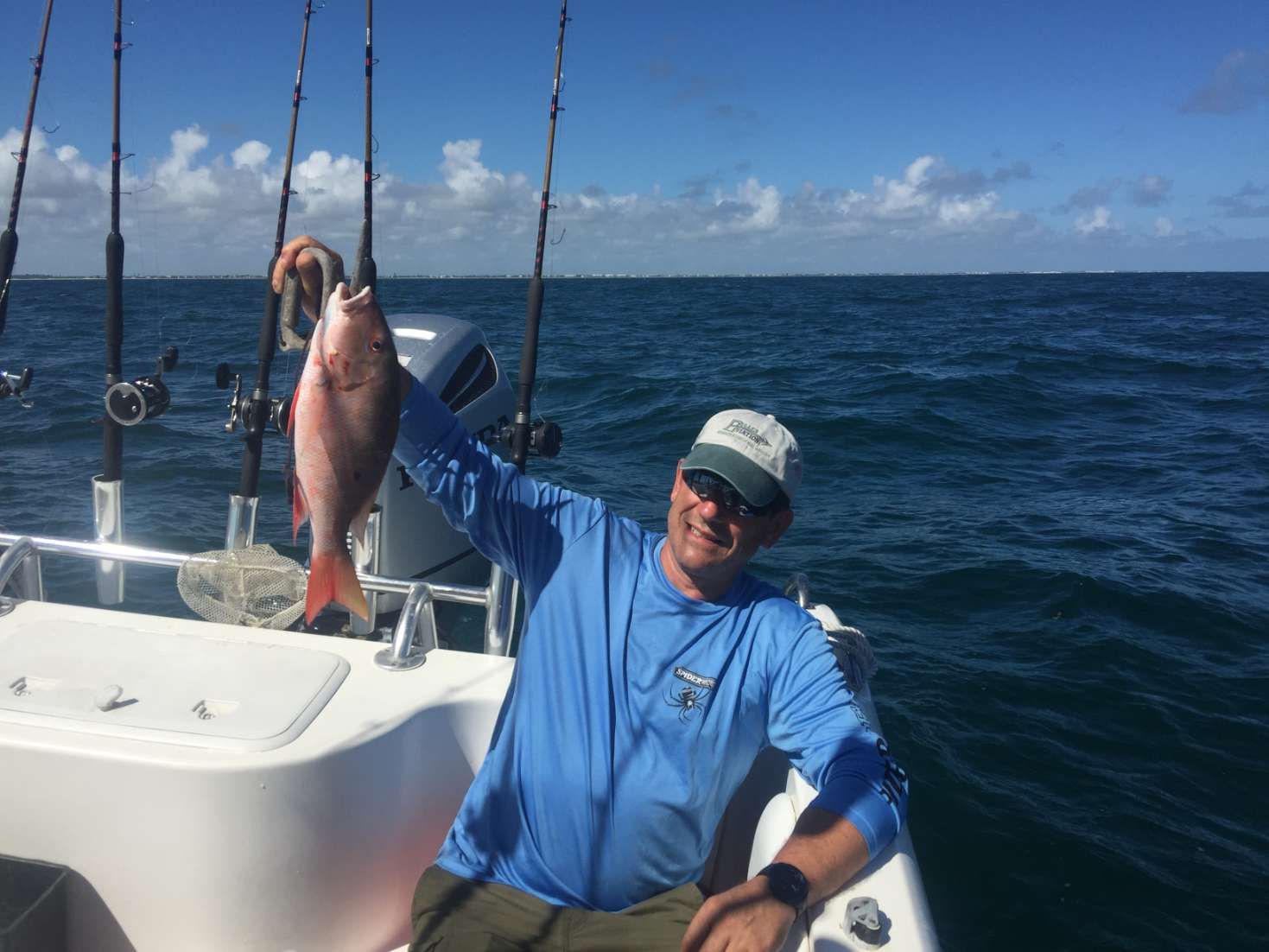 A man is holding a fish on a boat in the ocean.