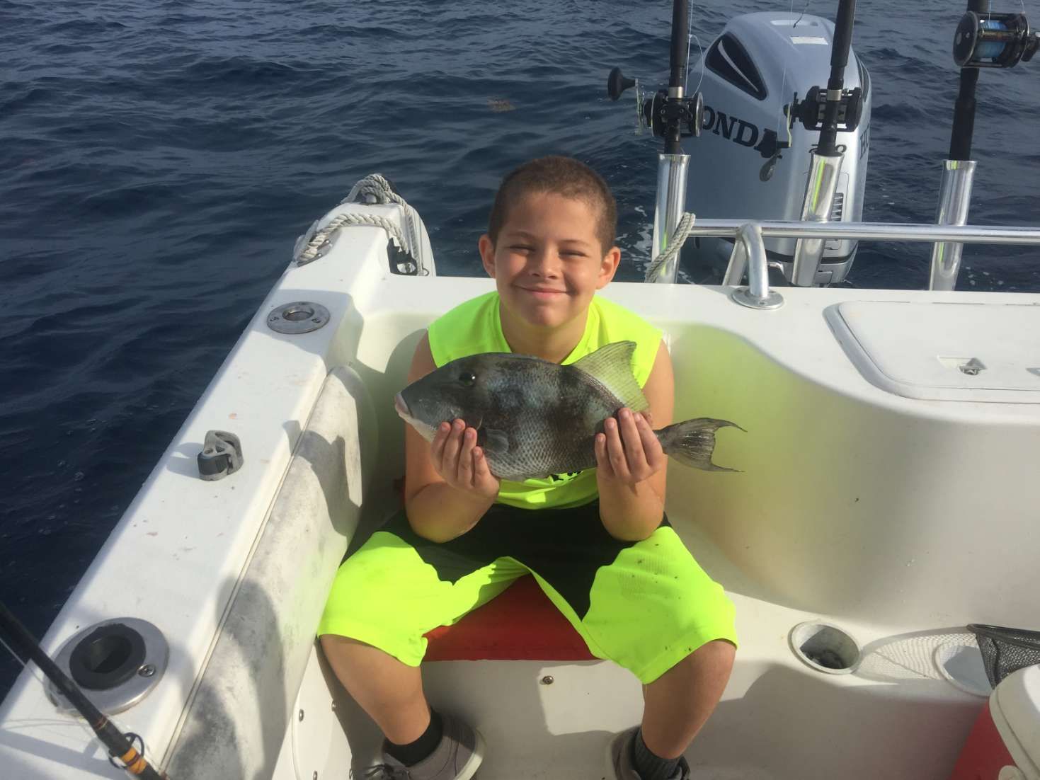 A young boy is sitting on a boat holding a fish.