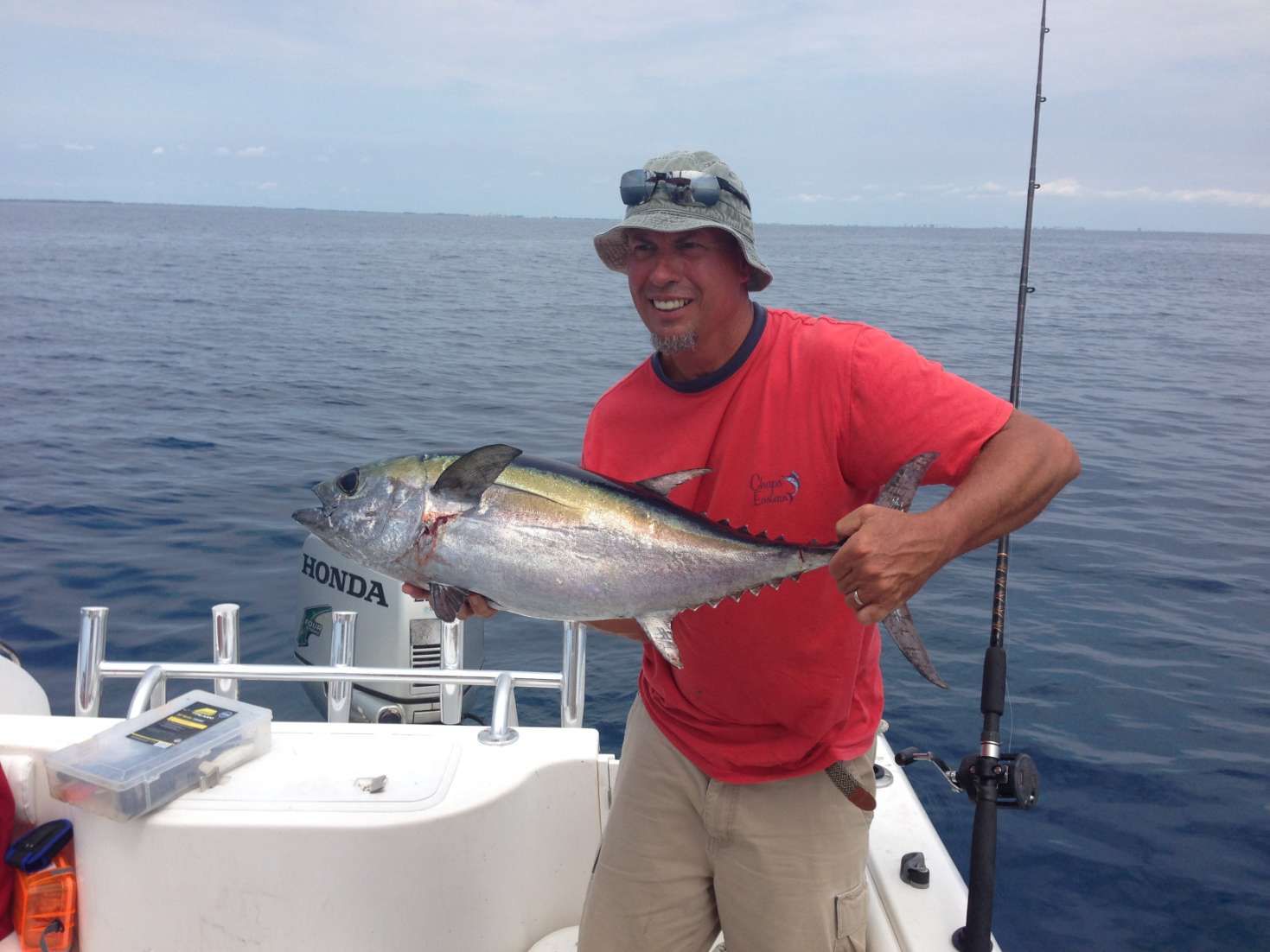 A man is holding a fish on a boat with a honda engine in the background