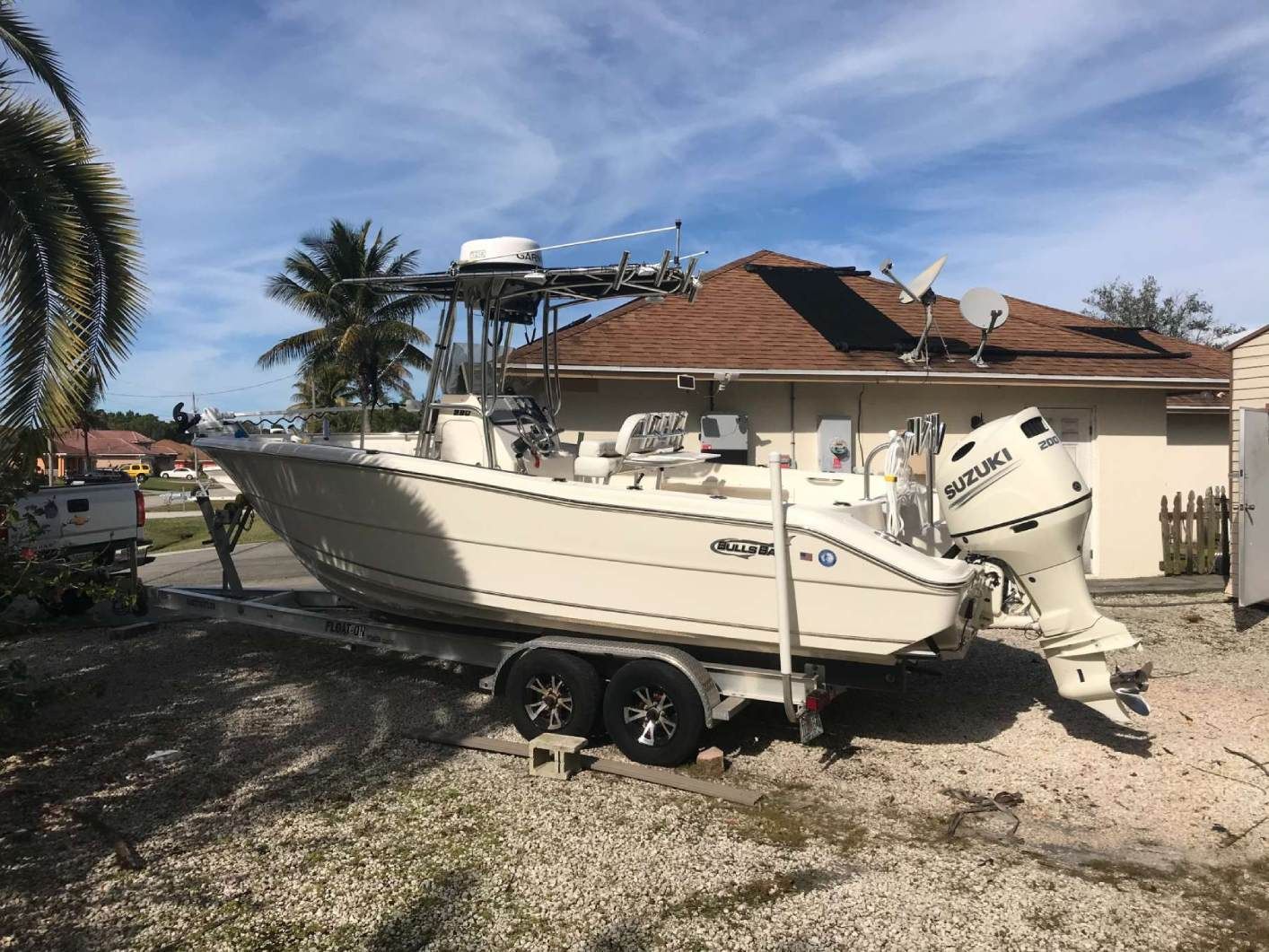 A white boat is parked on a trailer in front of a house.