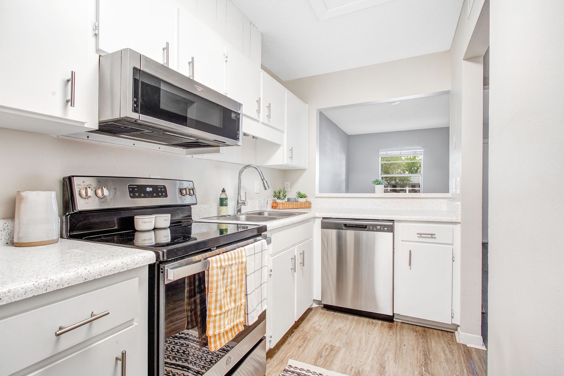 A kitchen with white cabinets , stainless steel appliances , a refrigerator , stove , sink and microwave.