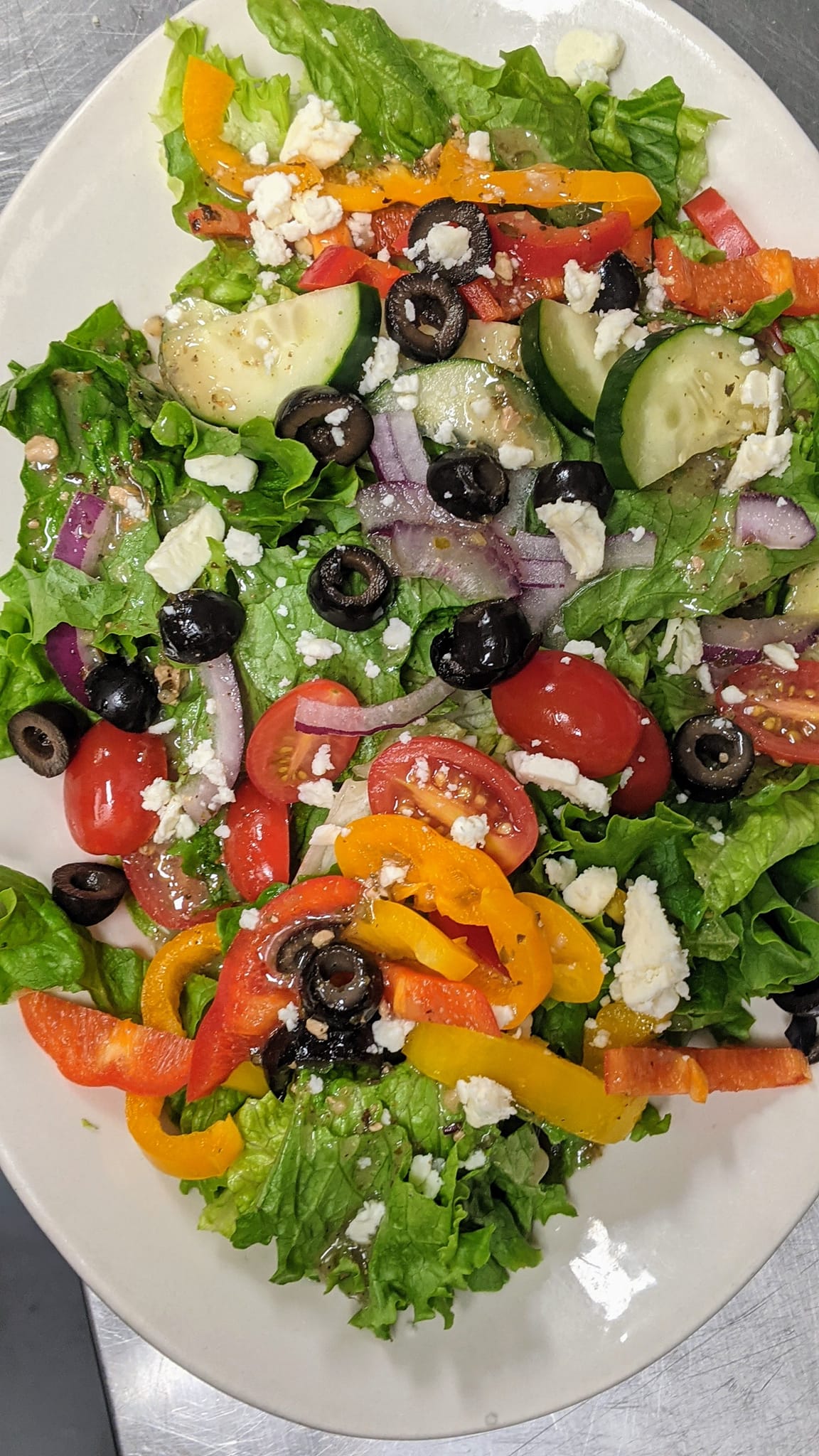 A white plate topped with a salad of lettuce , tomatoes , peppers , olives and feta cheese.