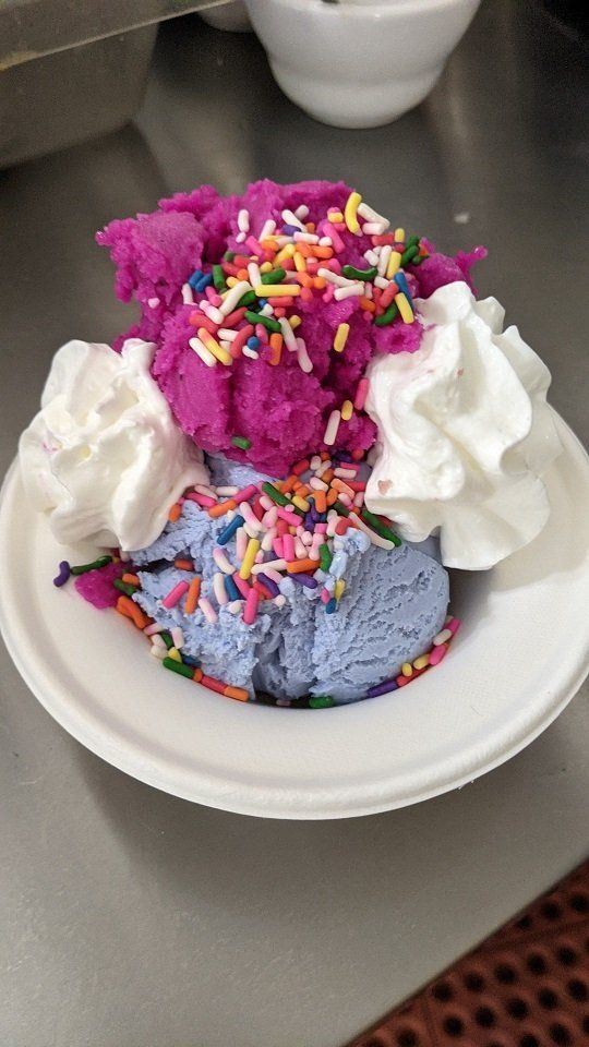 A bowl of ice cream with whipped cream and sprinkles on a table.
